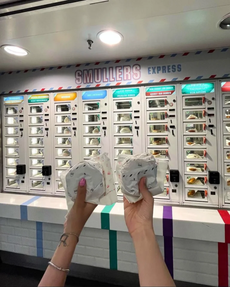 Bezoekers met twee verpakte snacks voor een ADM-snackmuur met de aanduiding Smullers Express