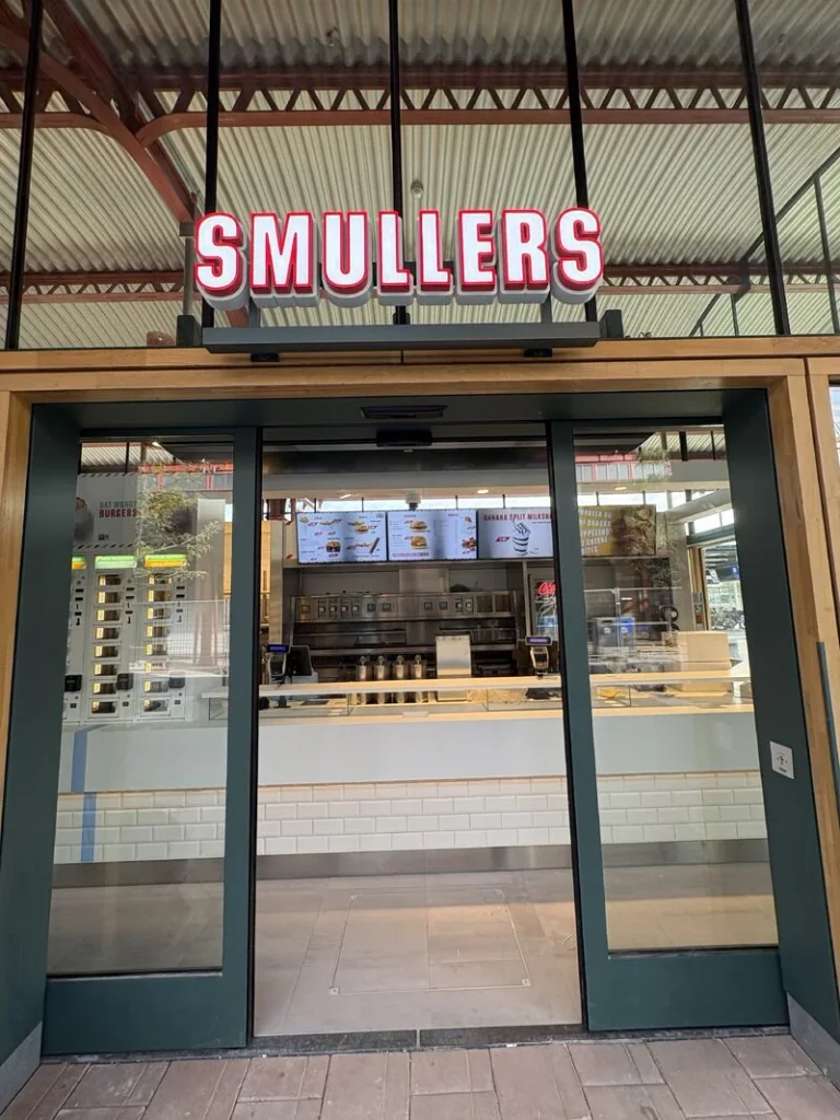De entree van een Smullers-locatie op een station, met de snackmuur zichtbaar naast de balie