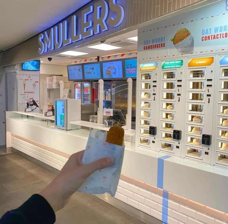 Een bezoeker houdt een kroket in een Smullers-verpakking vast, met de ADM-snackmuur op de achtergrond