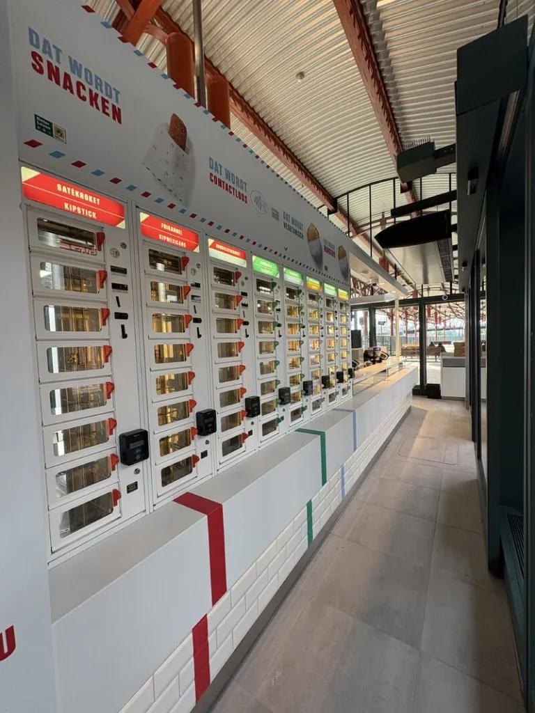 Een lange wand met ADM-loketautomaten naast de balie van een Smullers-stationslocatie